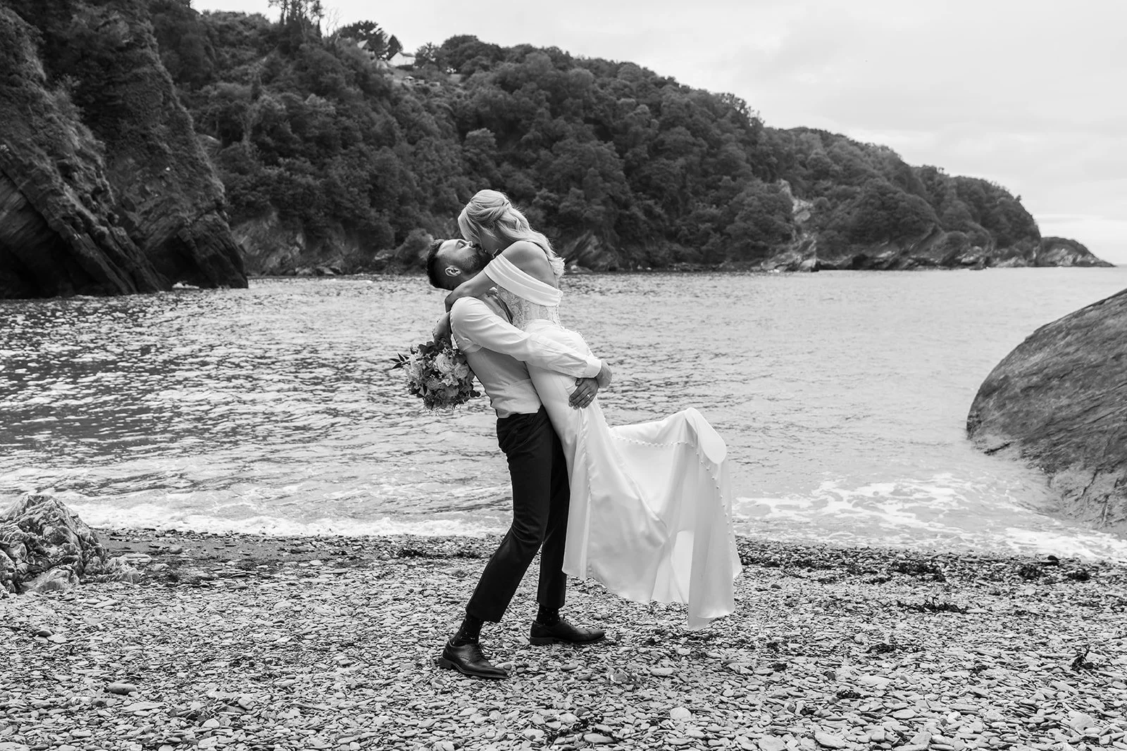 Black and white photo of Amy and Connor sharing a playful kiss on the beach during their Sandy Cove Hotel wedding in Devon, photographed by Just James Weddings.