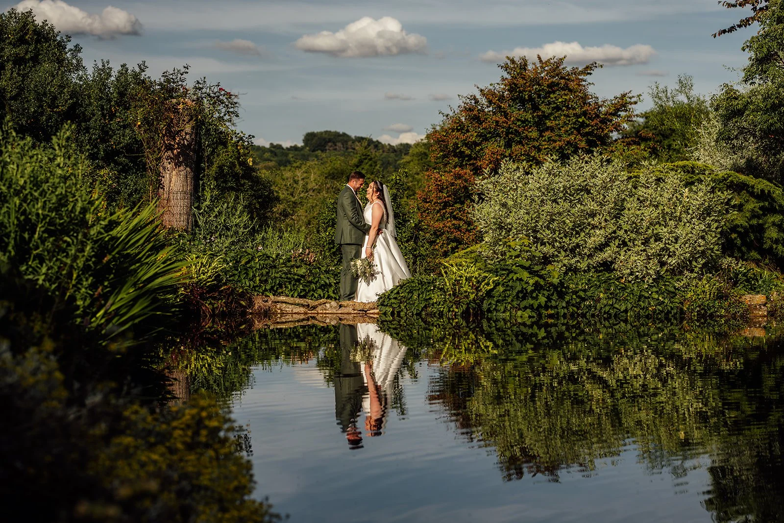 Chloe and Armani share a quiet moment beside the pond and lush gardens at The Barn at Upcote in Gloucestershire, photographed by Just James Weddings.