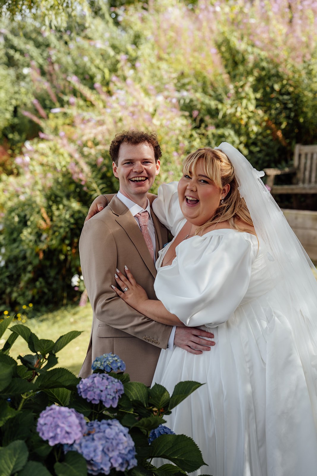 Holly & Alex laugh together during relaxed wedding portraits in the gardens at Sandy Cove Hotel in North Devon, photographed by Just James Weddings.