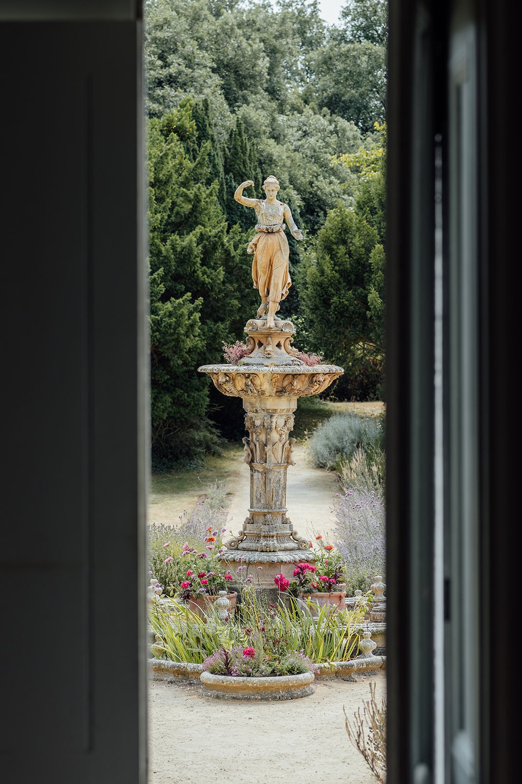 View of the ornate fountain in the formal gardens at Clevedon Hall in Somerset, framed through a doorway and photographed by Just James Weddings.