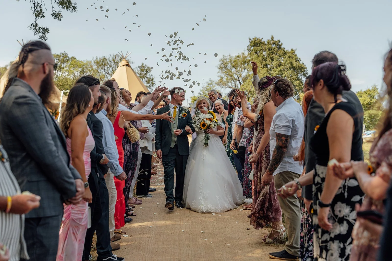 Lucy and Matthew walking hand in hand through confetti after their outdoor wedding ceremony at Curated Canvas at Noah’s Pond in Somerset, photographed by Just James Weddings.
