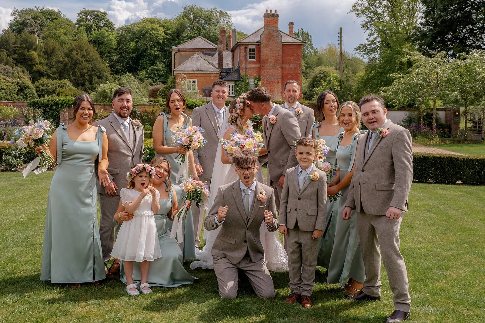 Jaye & Josh posing with their wedding party in the gardens at Syrencot in Wiltshire, photographed by Just James Weddings for relaxed and colourful group portraits.