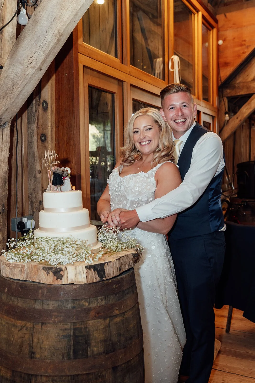 Elise and Tom cutting their wedding cake together inside the rustic barn at Bowerchalke Barn in Wiltshire, photographed by Just James Weddings.