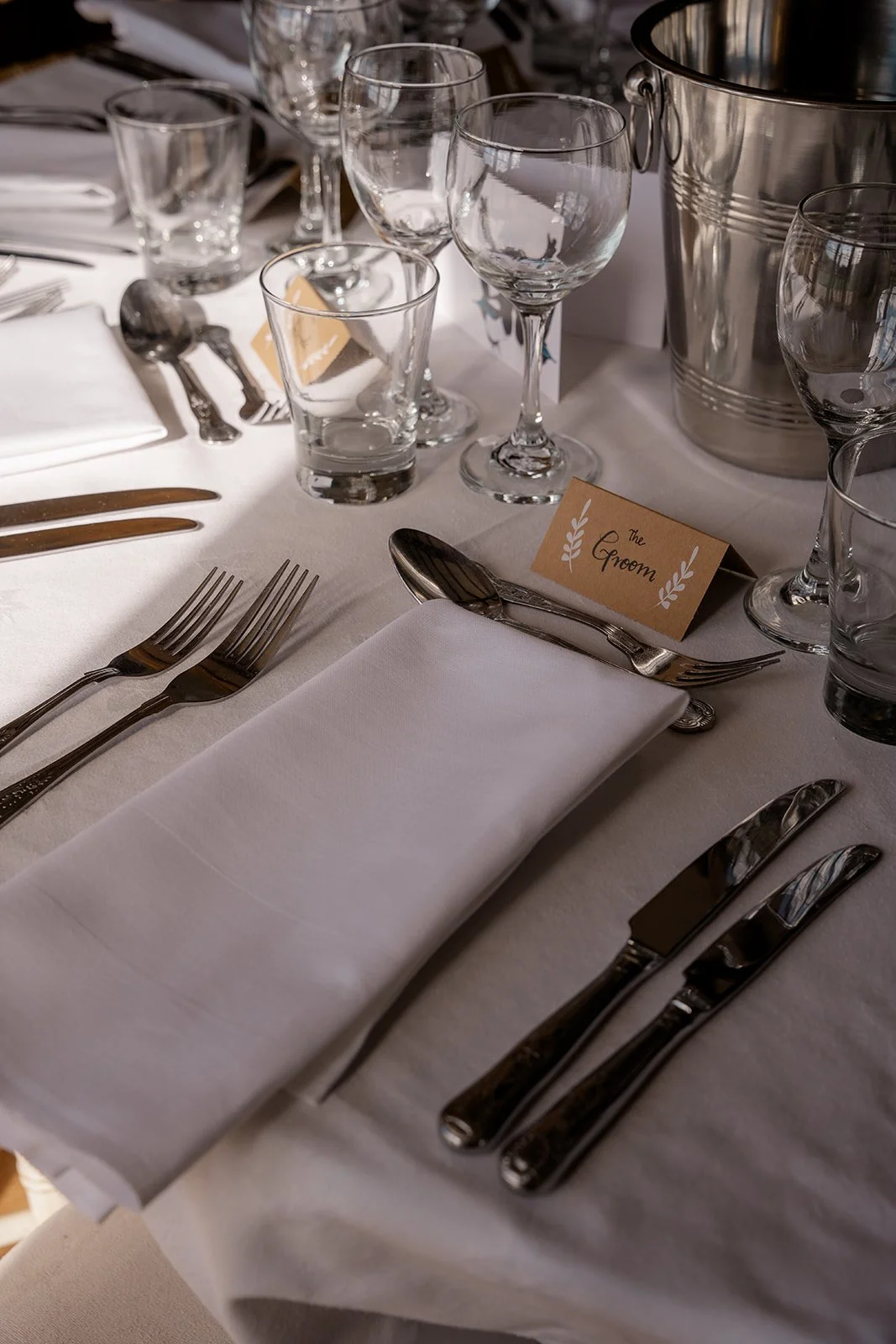 Close up of a wedding place setting at Broadfield Court in Herefordshire, with white linen, glassware, silver cutlery and a personalised name card, photographed by Just James Weddings.
