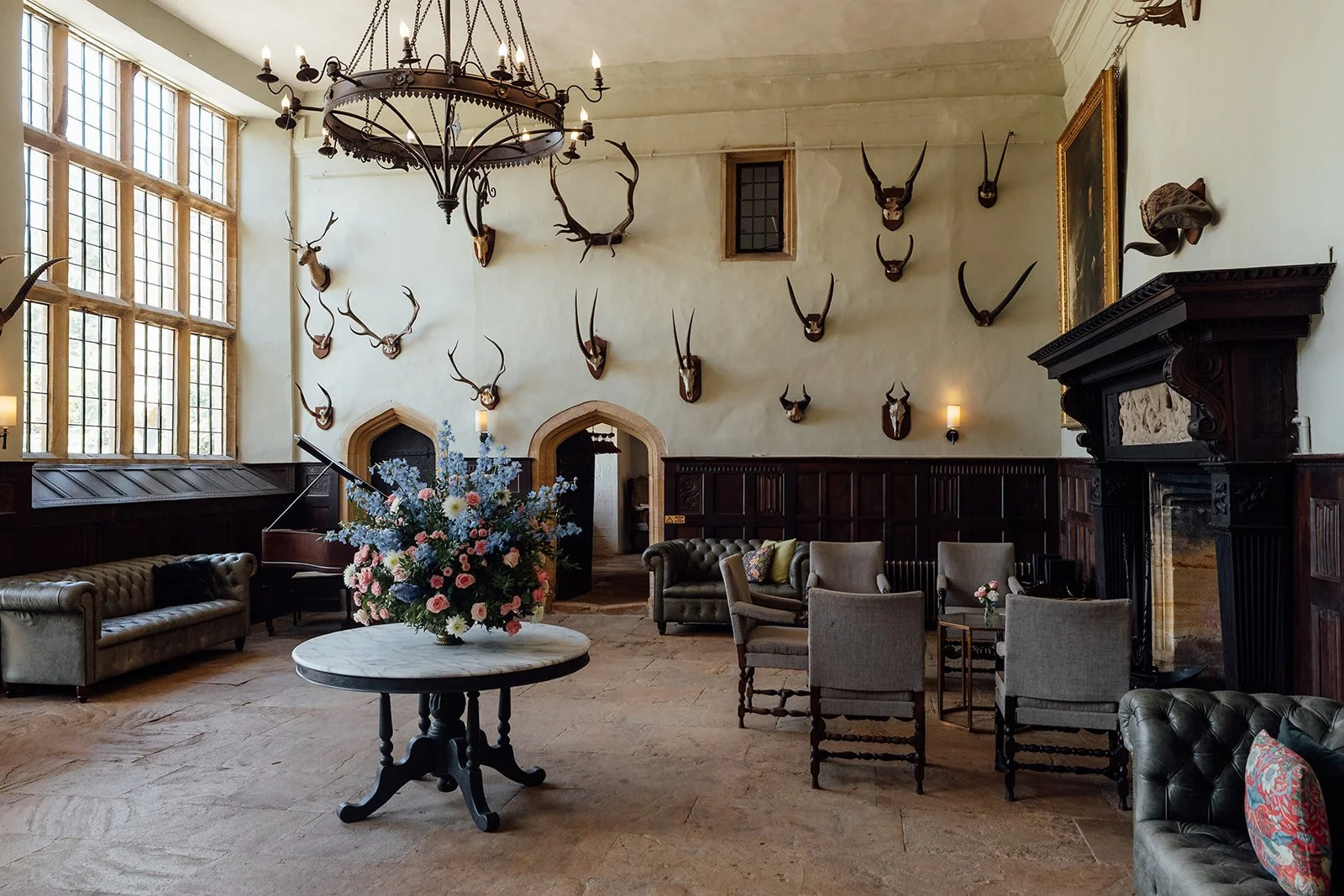 The Great Hall at Brympton House in Somerset, with historic wood panelling, large windows, mounted antlers, fireplace and floral centrepiece, photographed by Just James Weddings.