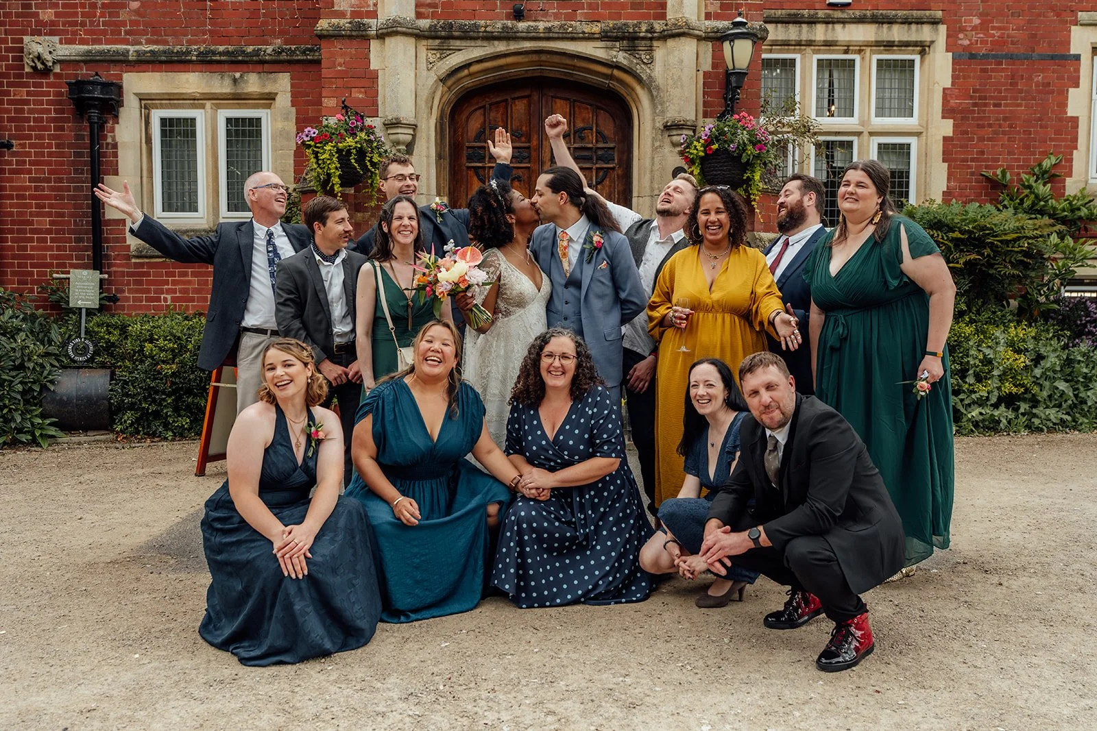 Melody & Jonny kiss while their wedding party laugh and celebrate around them outside Berwick Lodge in Bristol, photographed by Just James Weddings.