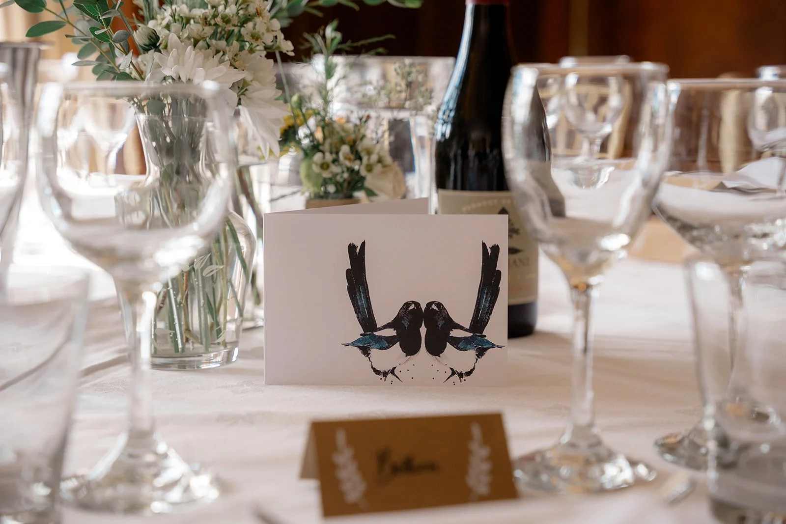 Wedding table detail at Broadfield Court in Herefordshire, with glassware, white flowers and illustrated bird stationery, photographed by Just James Weddings for reception decor inspiration.