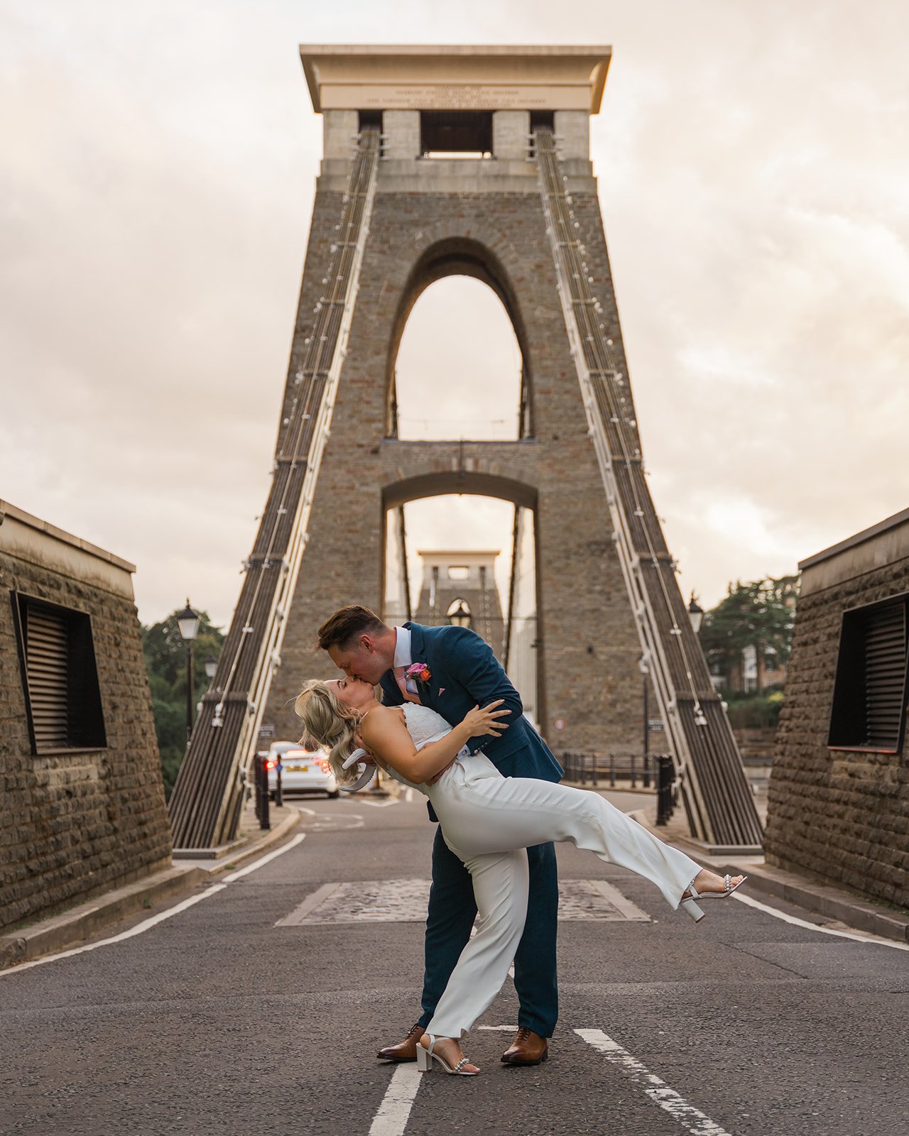Kristy and Will share a playful dip and kiss on Clifton Suspension Bridge in Bristol, UK, creating a dramatic wedding portrait after their celebration at No. 4 Clifton Village.