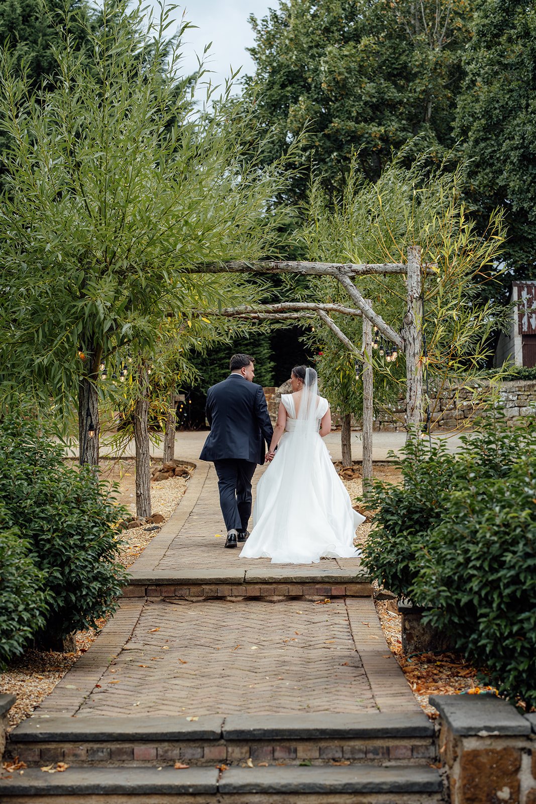 Harriet & Simon walk hand in hand through the landscaped grounds at Dovecote Events in Oxfordshire, photographed by Just James Weddings.