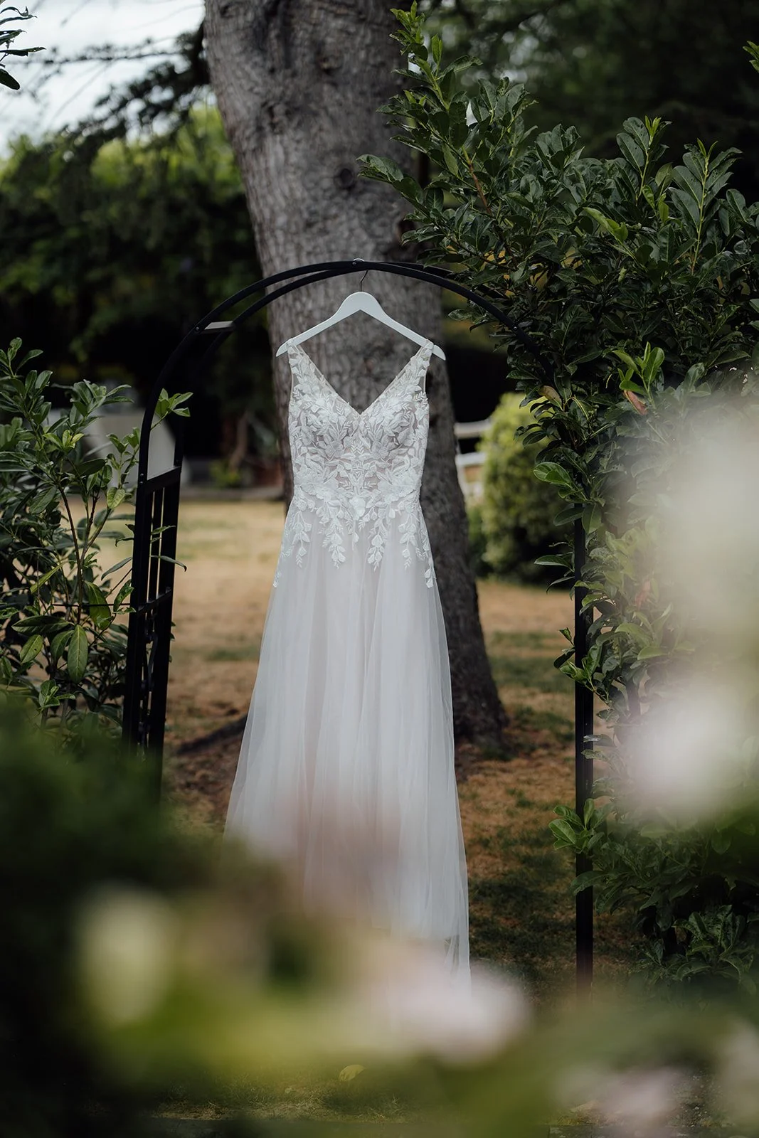Kasey and Larisha’s lace wedding dress hanging outdoors among the greenery at Oaks Farm Weddings in Surrey, photographed before their wedding ceremony.