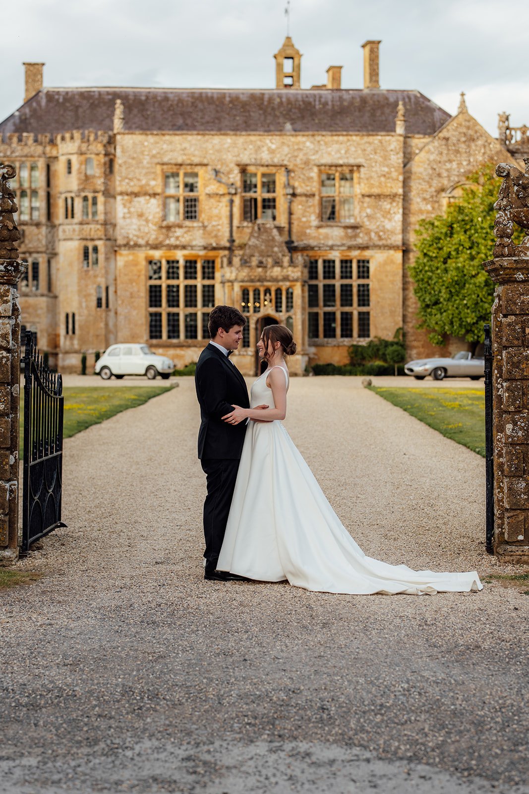 Rachel & Tom stand together on the gravel drive in front of Brympton House in Somerset, with the historic manor behind them, photographed by Just James Weddings.