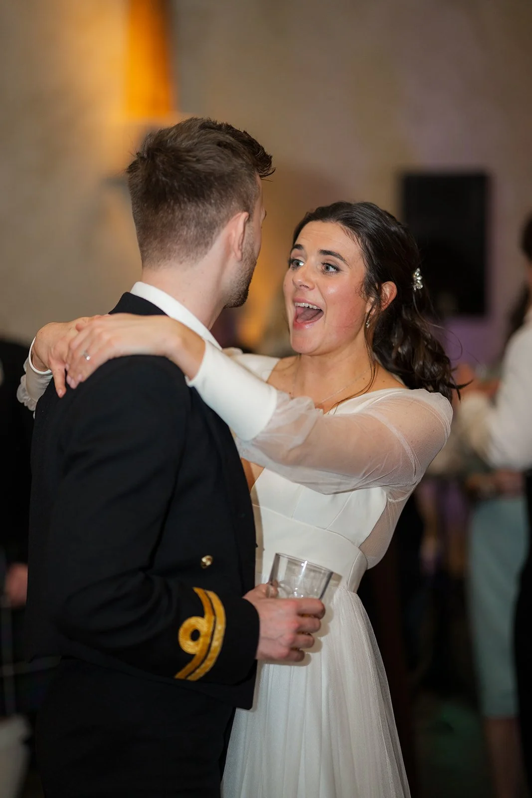Megan & Luca share a lively dance inside The Great Barn Devon during their wedding reception, with Megan smiling mid-song as she wraps her arms around Luca. Warm lighting and blurred guests create an energetic Devon celebration scene.