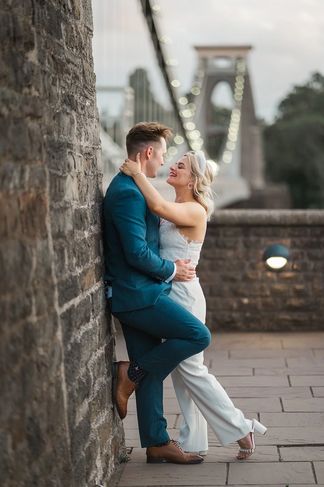 Kristy and Will embrace beside a stone wall near Clifton Suspension Bridge in Bristol, UK, sharing a romantic moment during their No. 4 Clifton Village wedding portraits.