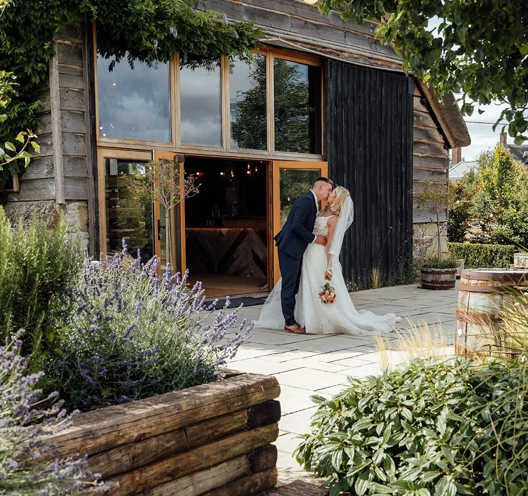 Elise and Tom sharing a kiss outside the rustic barn during their Bowerchalke Barn wedding in Wiltshire, photographed by Just James Weddings.