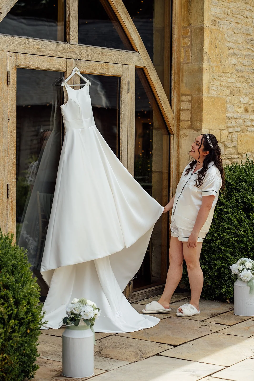 Chloe standing beside her wedding dress outside The Barn at Upcote in the Cotswolds, photographed by Just James Weddings for relaxed bridal preparation and wedding morning details.