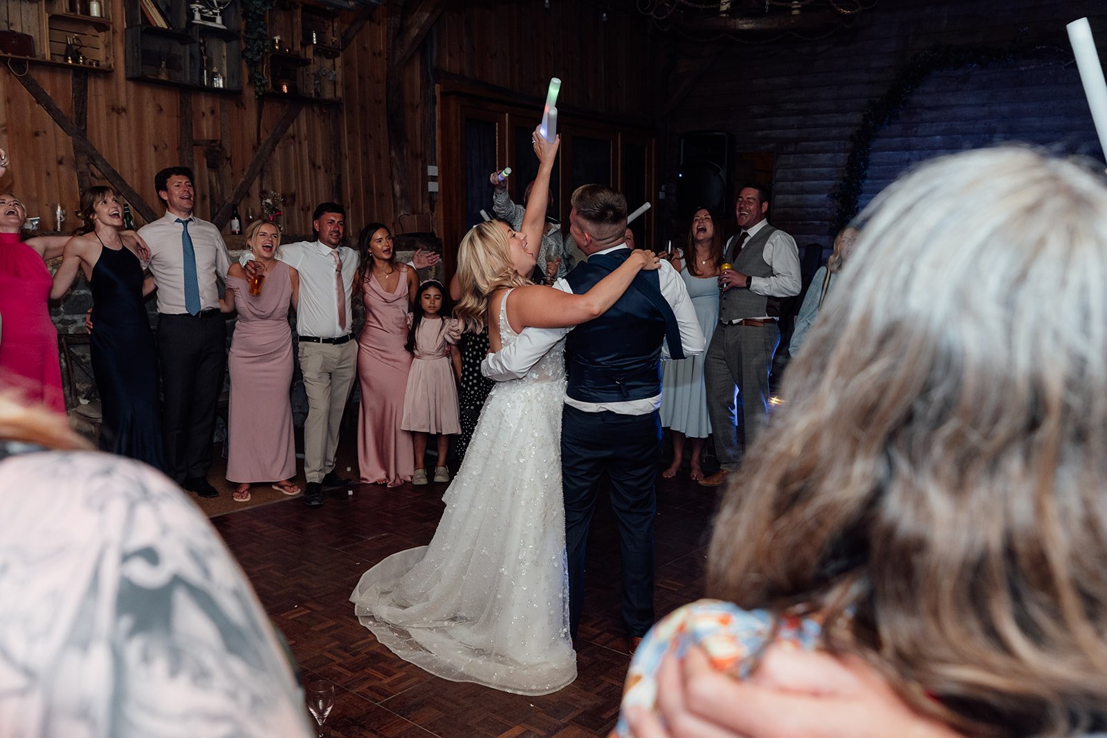 Elise and Tom dancing together as wedding guests sing and celebrate around them during the evening reception at Bowerchalke Barn in Wiltshire, photographed by Just James Weddings.