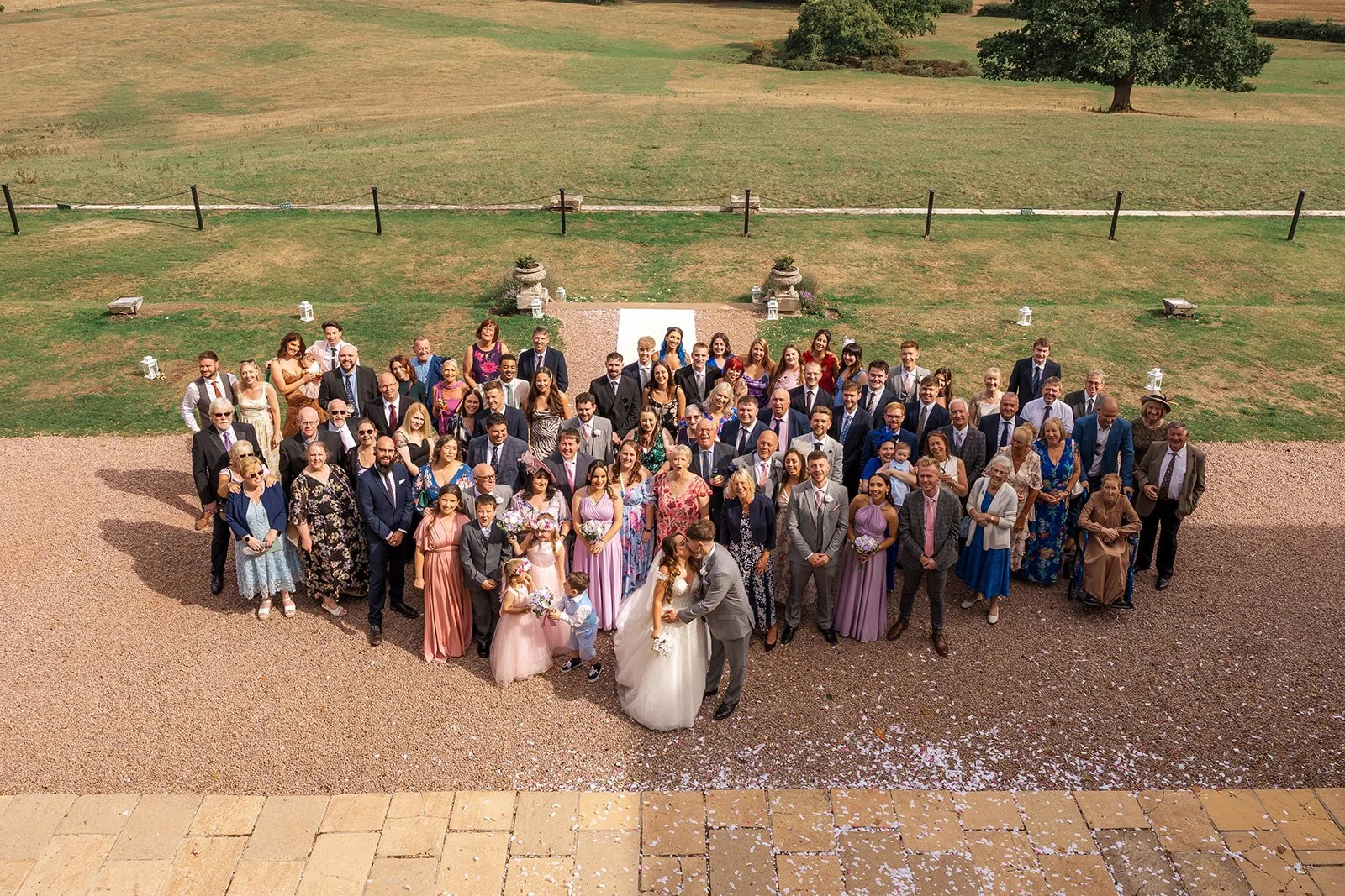 Aerial group photo of Rhiannon & Anthony with their wedding guests outside Eastwood Park in Gloucestershire, photographed by Just James Weddings after the ceremony.