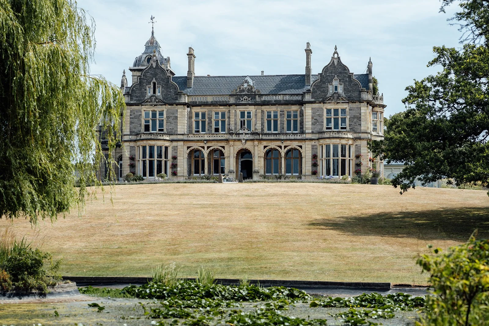 Exterior view of Clevedon Hall in Somerset, showing the historic manor house, lawn and surrounding gardens, photographed by Just James Weddings.
