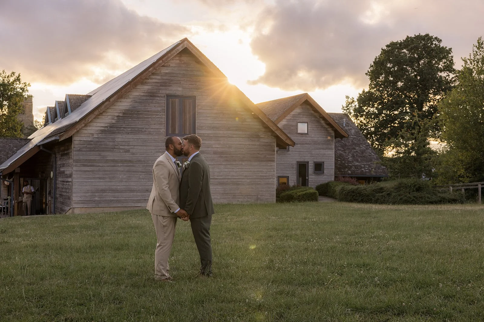 Aaron & Jack share a kiss while holding hands during golden-hour portraits outside Rock Village Hall in Worcestershire, photographed by Just James Weddings.