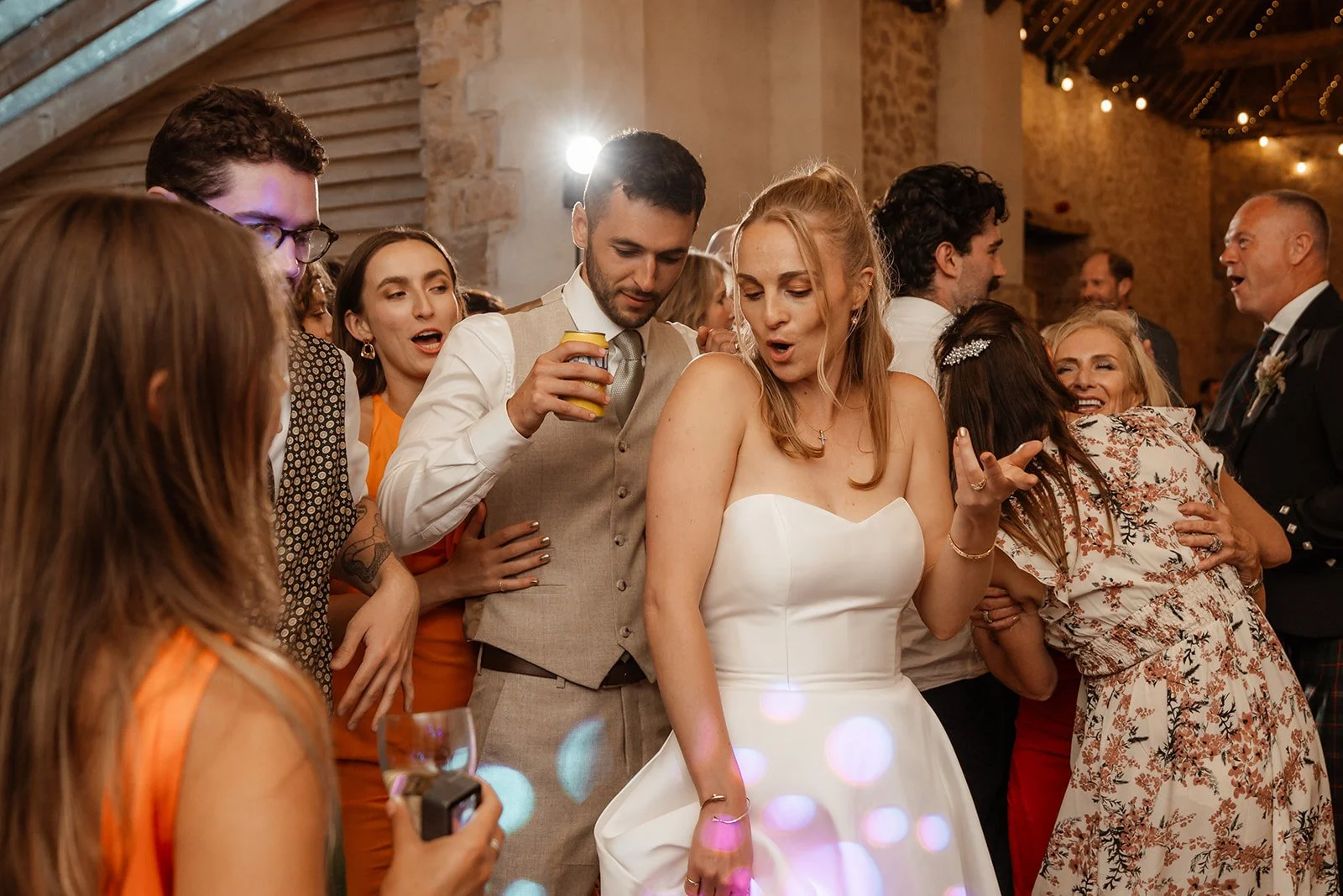 Louise & Christian dancing with guests inside The Cider Barn in Somerset, with party lights, drinks and a packed dance floor, photographed by Just James Weddings for lively wedding reception moments.