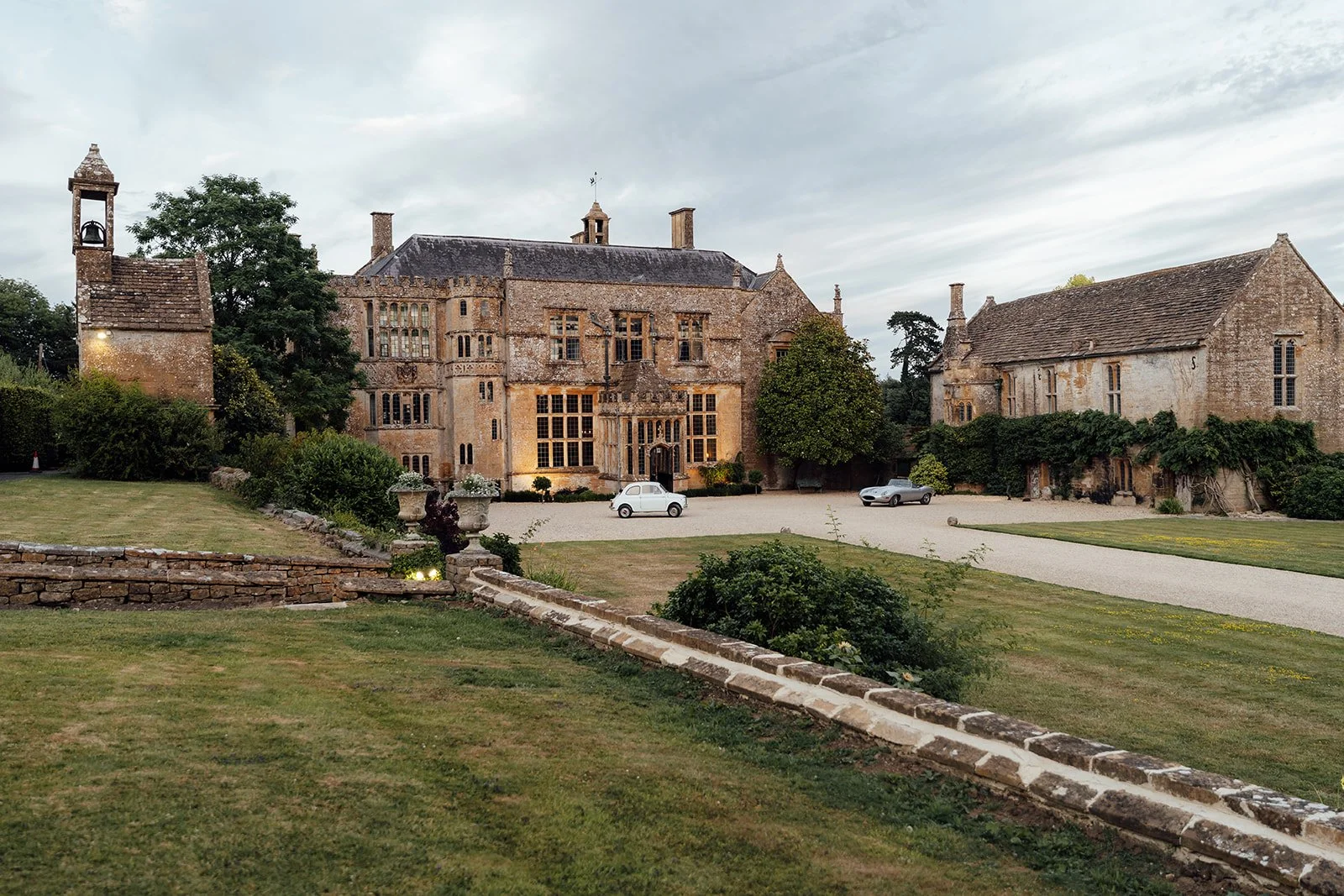 Wide exterior view of Brympton House in Somerset, showing the historic manor, surrounding buildings, gravel courtyard and landscaped grounds, photographed by Just James Weddings.