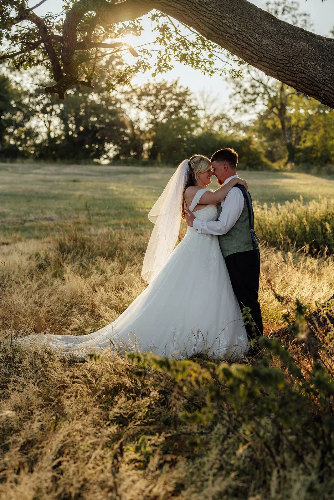 Lucy and Matthew sharing a quiet embrace beneath a large tree during golden hour wedding portraits at Curated Canvas at Noah’s Pond in Somerset, photographed by Just James Weddings.