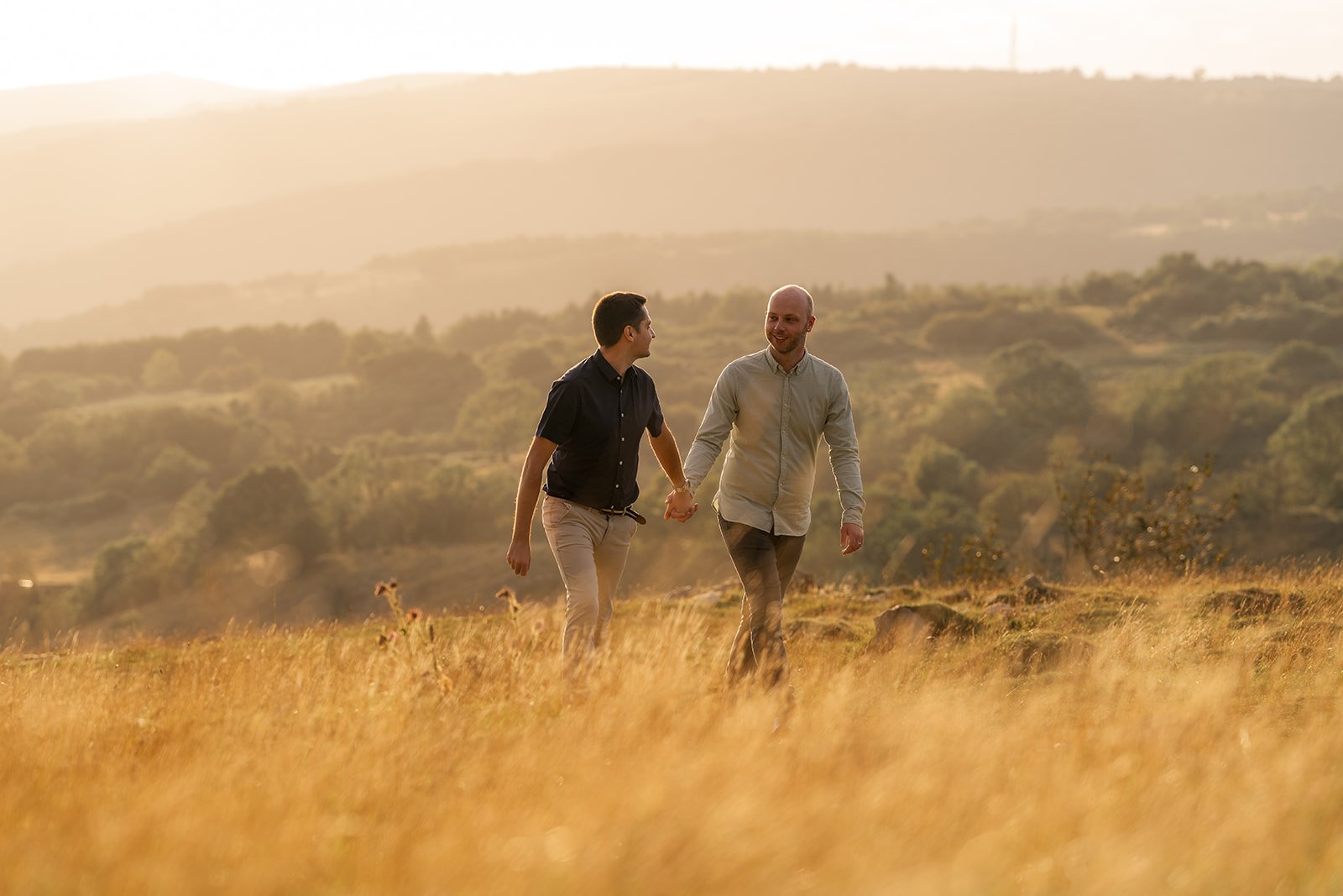 Photo of a gay couple who are newly engaged walking hand in hand at golden hour overlooking Cheddar Gorge in Somerset