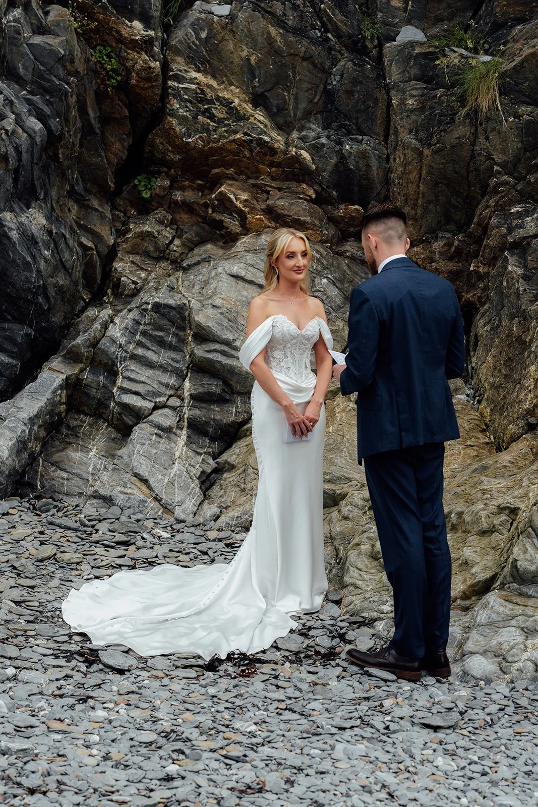 Amy & Connor exchange personal vows beside dramatic rocks on the beach during their wedding portraits near Sandy Cove Hotel in North Devon, UK.