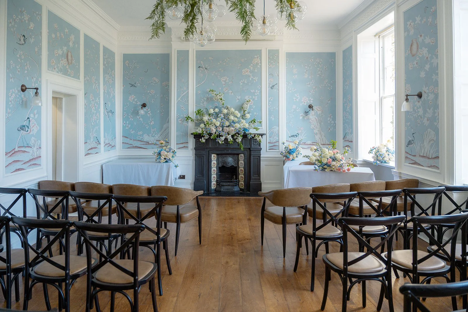 Wedding ceremony room at No. 4 Clifton Village in Bristol, UK, decorated with pastel blue and white flowers, botanical wallpaper and wooden chairs ready for Ruth and Carmelo’s ceremony.