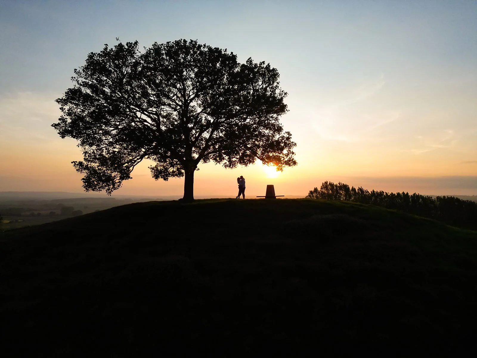 Drone photo of a newly engaged couple up the top of a hill at sunset doing an engagement photoshoot