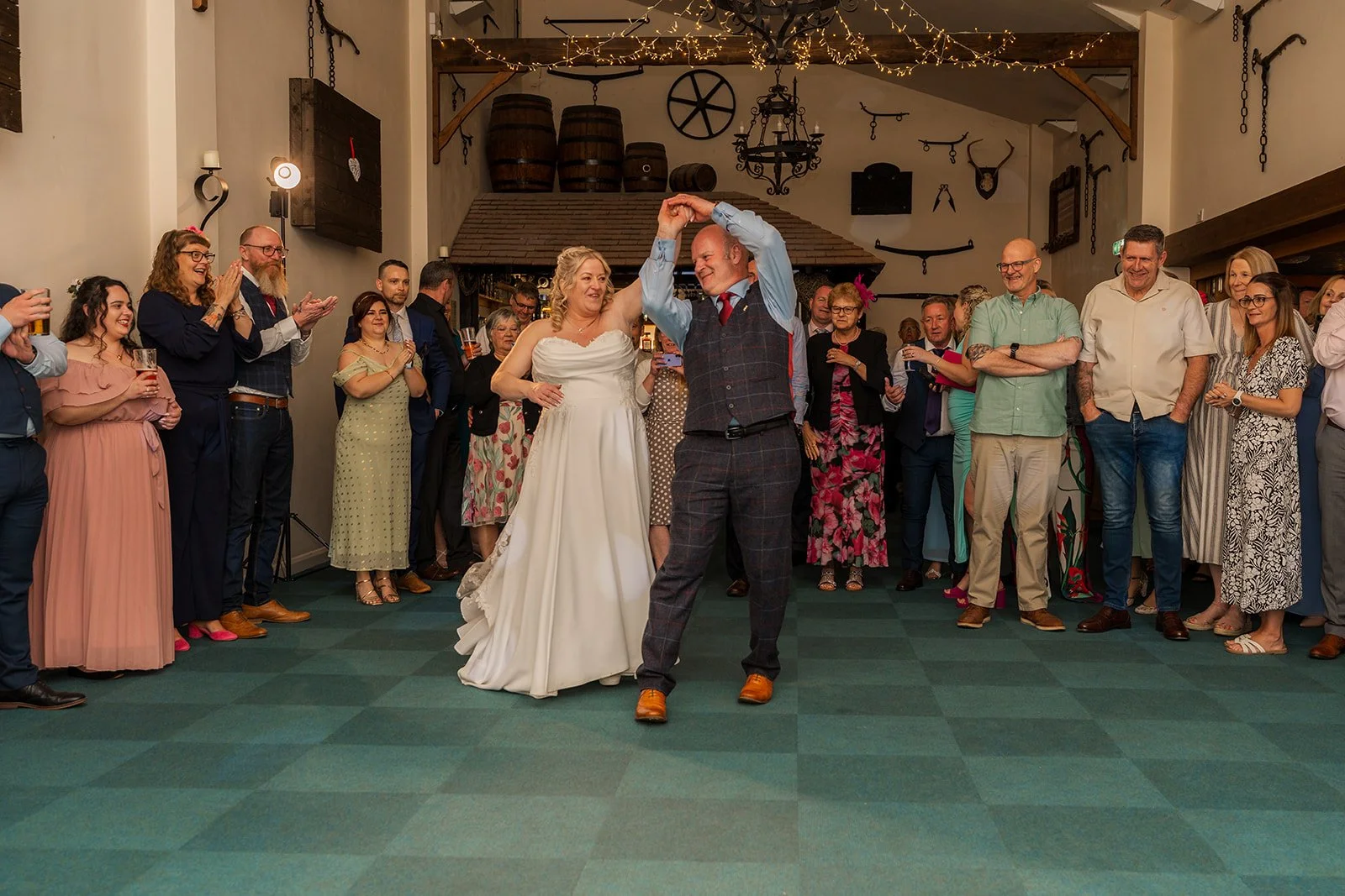Debbie and Nigel enjoy their first dance at Yarlington Barn in Somerset, surrounded by smiling guests, fairy lights and rustic barn details, capturing a joyful reception moment during their relaxed countryside wedding.