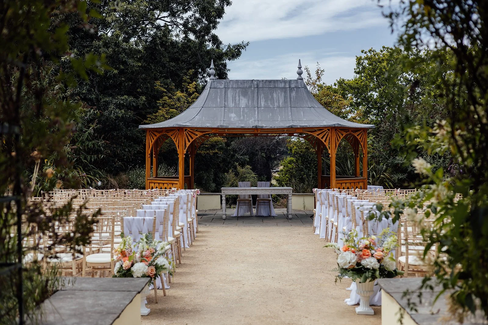 Outdoor ceremony setup at Clevedon Hall in Somerset, with rows of chairs, floral aisle details and a wooden gazebo surrounded by gardens, photographed by Just James Weddings.