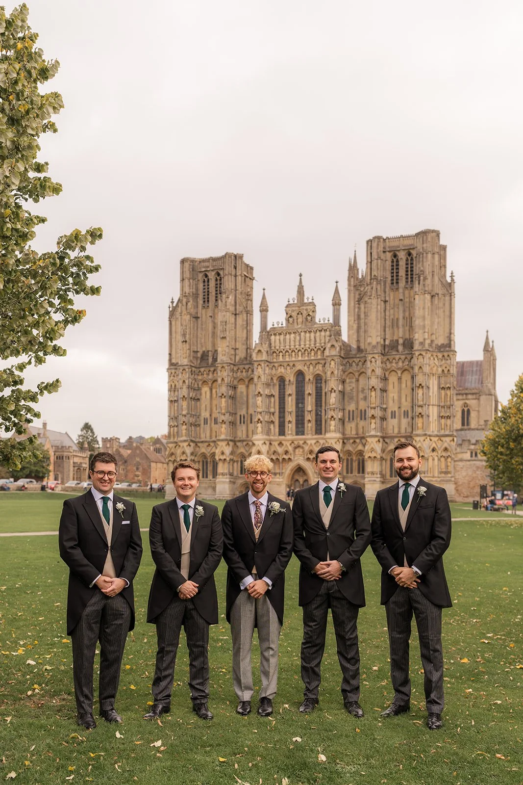 Iona & Will’s groomsmen stand on the lawn at Bishop’s Palace in Somerset, UK, posing in formal morning suits with Wells Cathedral rising behind them, creating a timeless wedding party portrait in an iconic Somerset setting on the wedding day.