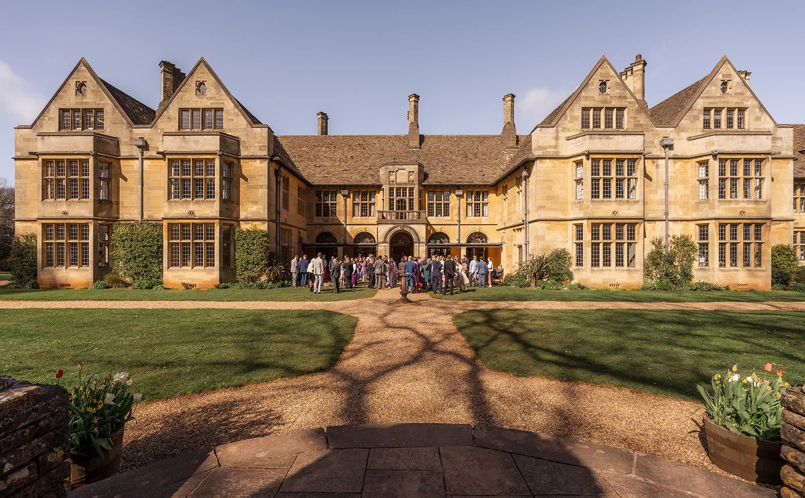 Exterior view of Coombe Lodge in Somerset, UK, showing the historic country house, landscaped gardens and wedding guests gathered outside on a sunny day.