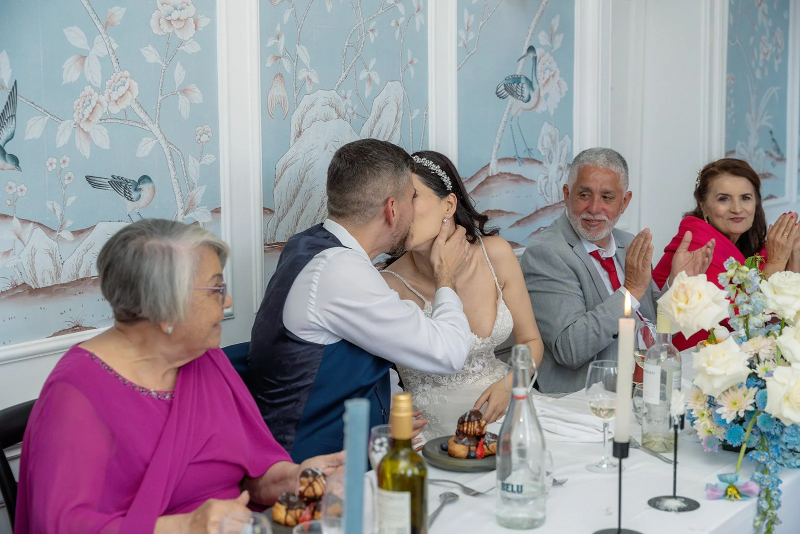 Ruth and Carmelo share a kiss during their wedding breakfast at No. 4 Clifton Village in Bristol, UK, surrounded by family, flowers and elegant table details.