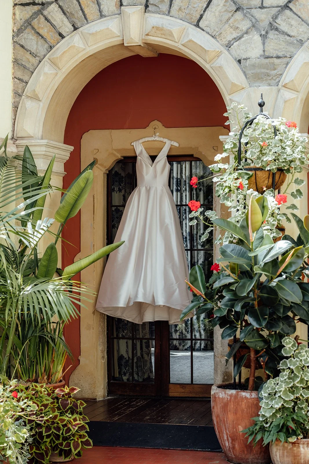 Caitlin’s satin wedding dress hanging beneath a stone archway at Clevedon Hall in Somerset, surrounded by lush greenery and flowering plants before her wedding to Kevin.