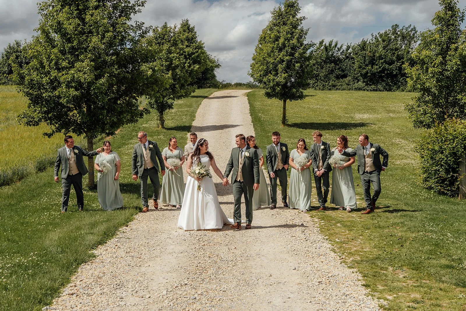 Chloe & Armani walking with their wedding party along the country drive at The Barn at Upcote in the Cotswolds, photographed by Just James Weddings for relaxed group portraits.