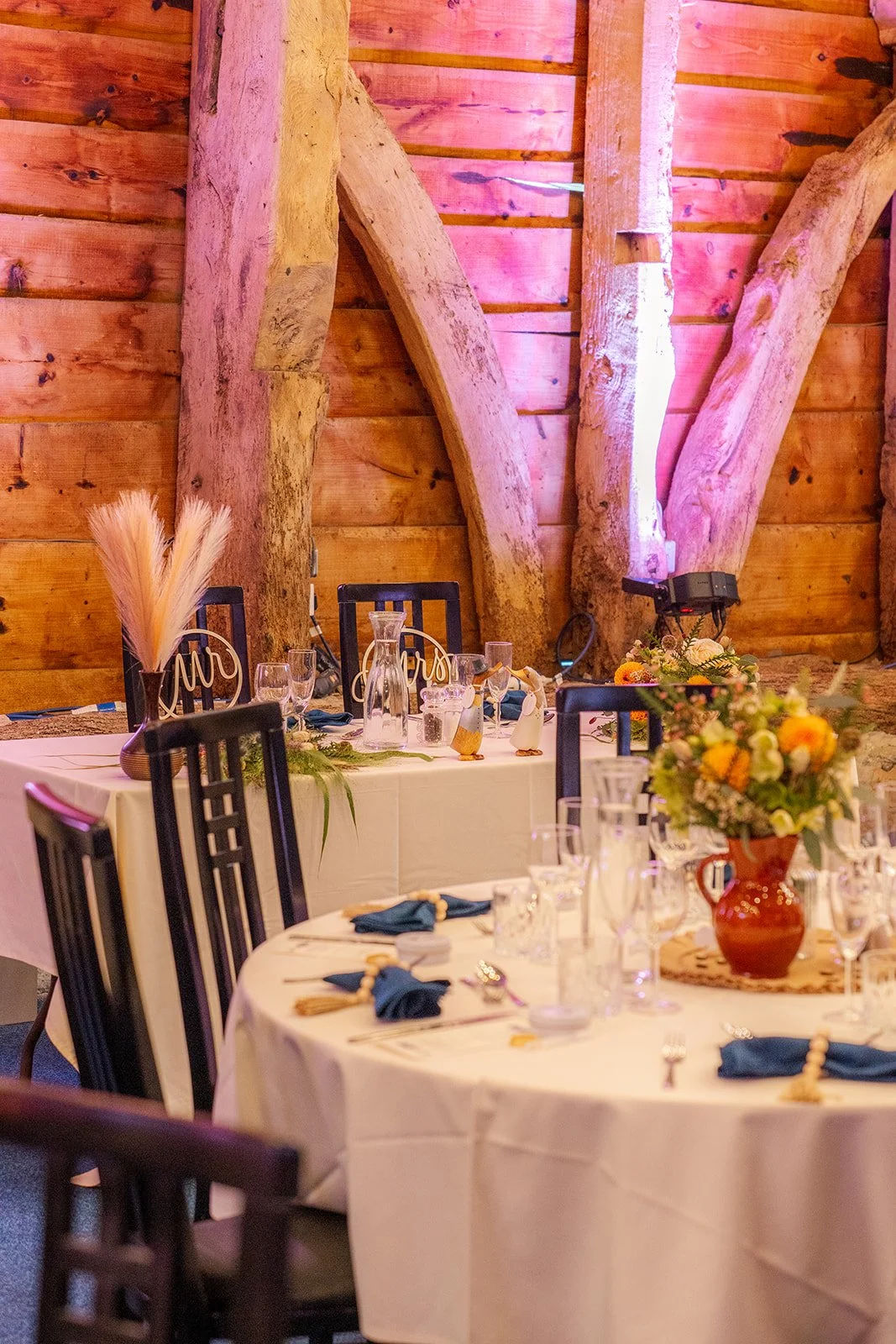 Wedding breakfast tables inside Stockbridge Farm Barn in Dorset, with rustic beams, autumn flowers, candles and warm lighting, photographed by Just James Weddings for seasonal reception decor inspiration.