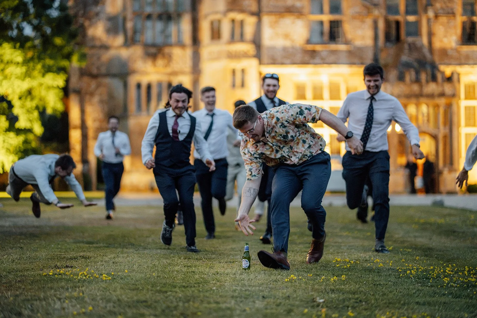 Wedding guests run across the lawn during an outdoor game in front of Brympton House in Somerset, photographed by Just James Weddings.