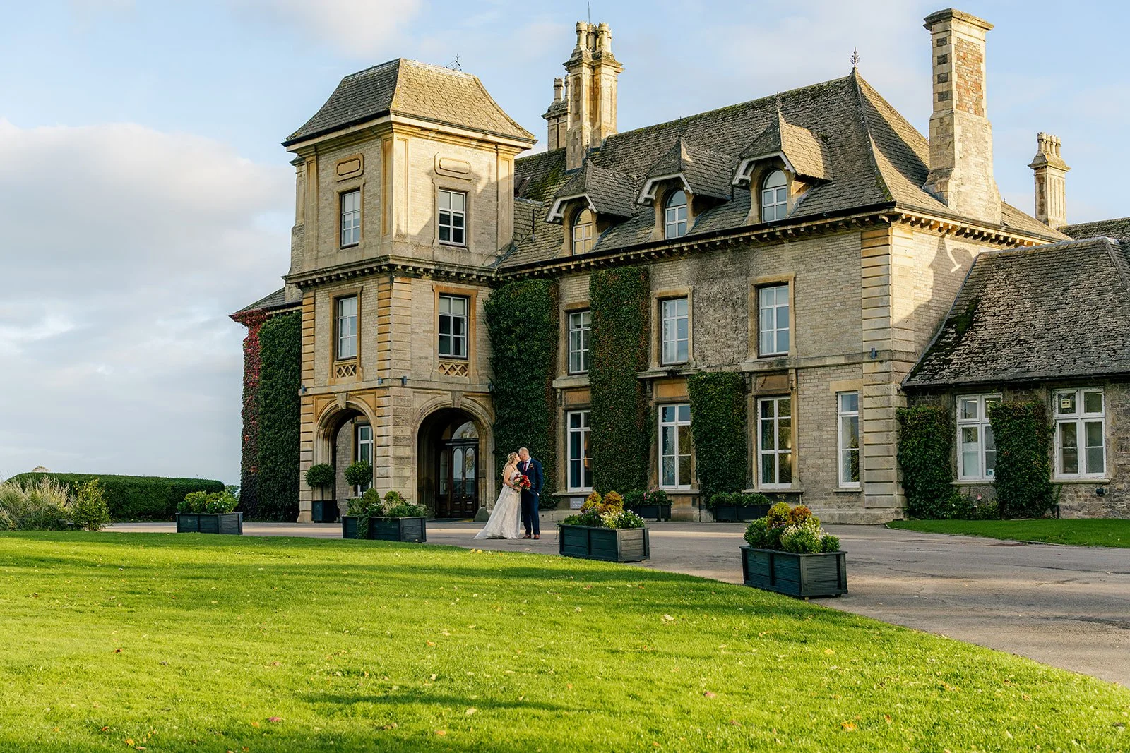 Lucy & Jay share a quiet moment during their wedding at Eastwood Park in Gloucestershire, UK, standing together in front of the grand manor house with ivy-covered stone walls and landscaped gardens.