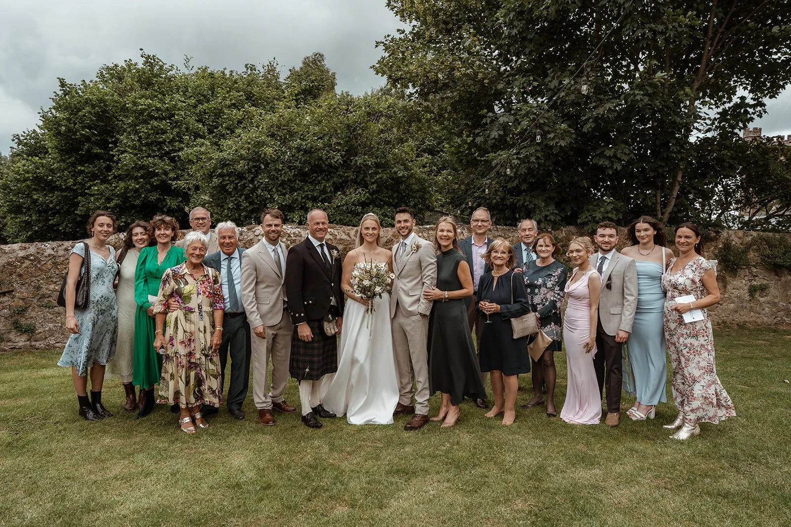 Louise & Christian standing with family for a group photo at The Cider Barn in Somerset, photographed by Just James Weddings for relaxed countryside wedding photography with guests outdoors.