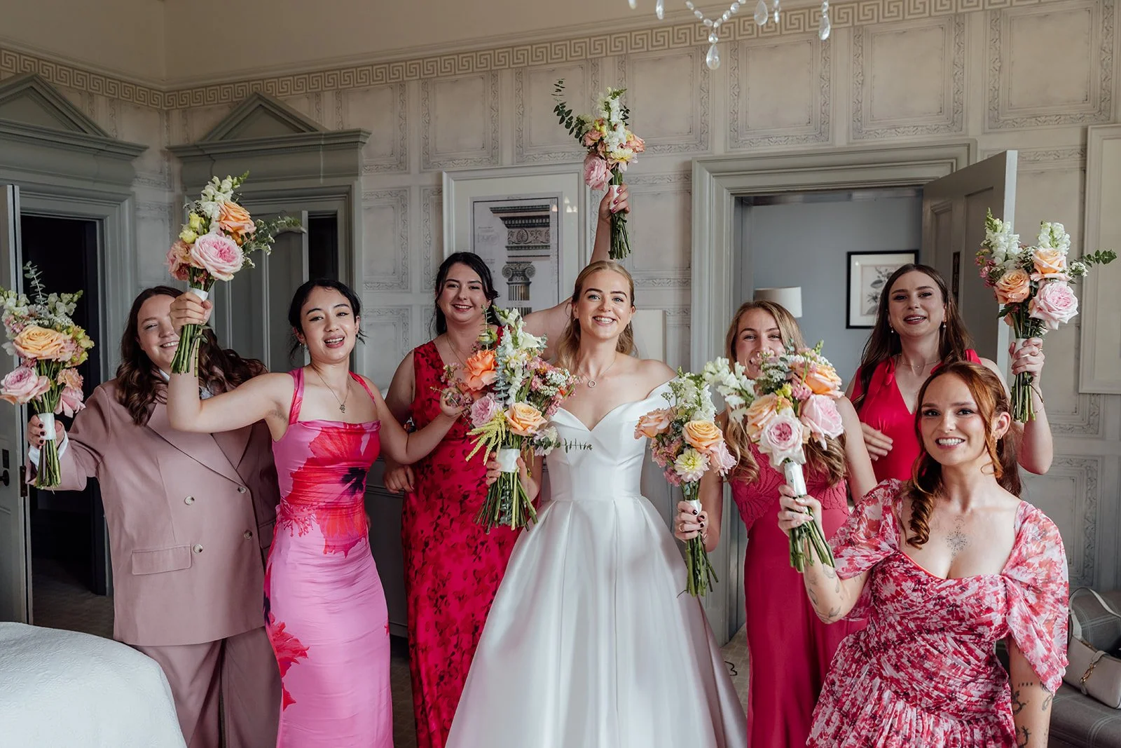 Caitlin celebrating with her bridesmaids at Clevedon Hall in Somerset, holding colourful bouquets and wearing pink dresses, photographed by Just James Weddings.