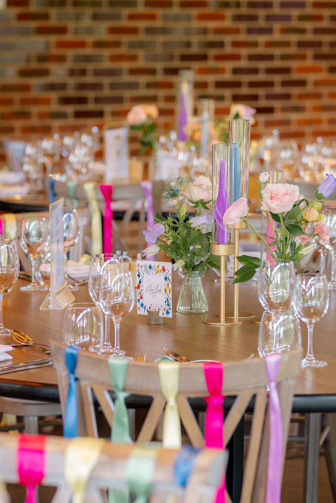 Close up of wedding table styling at Syrencot in Wiltshire, with pastel flowers, candles, glassware and colourful ribbons, photographed by Just James Weddings for reception decor inspiration.