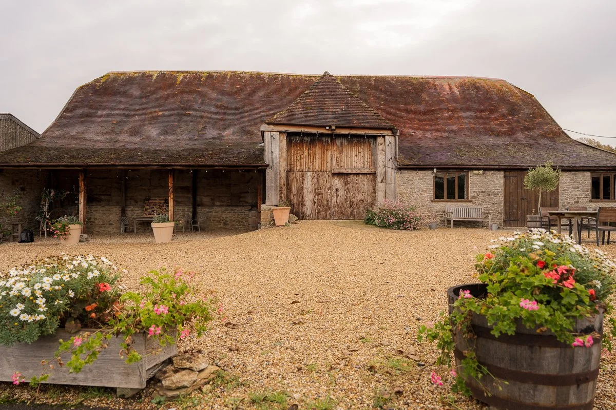 Stockbridge Farm Barn in dorset on Maisie & Andrew’s wedding day, showing the rustic stone barn, wooden doors, and gravel courtyard framed by flower planters. A countryside venue with warm tones and a relaxed rural atmosphere.