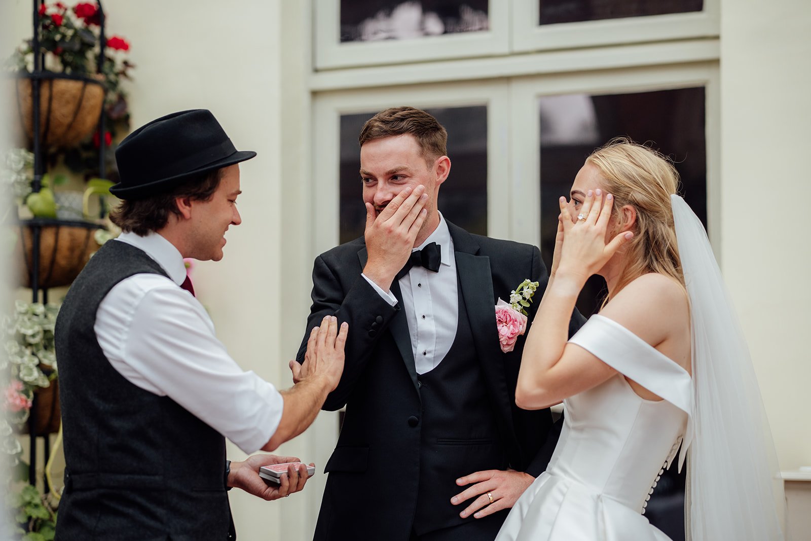 Caitlin and Kevin reacting with surprise during a magician’s card trick at their Clevedon Hall wedding in Somerset, sharing a fun candid moment during the reception.