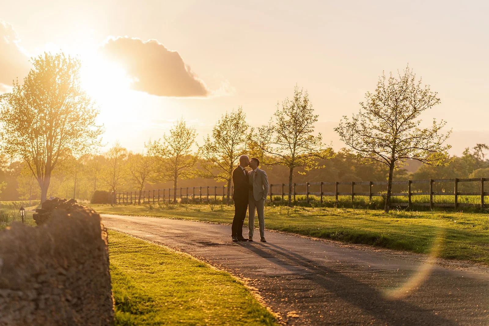 Sam & Gavin standing together on the lane at sunset at The Great Barn at Aynho in the Cotswolds, photographed by Just James Weddings for golden hour wedding portraits.