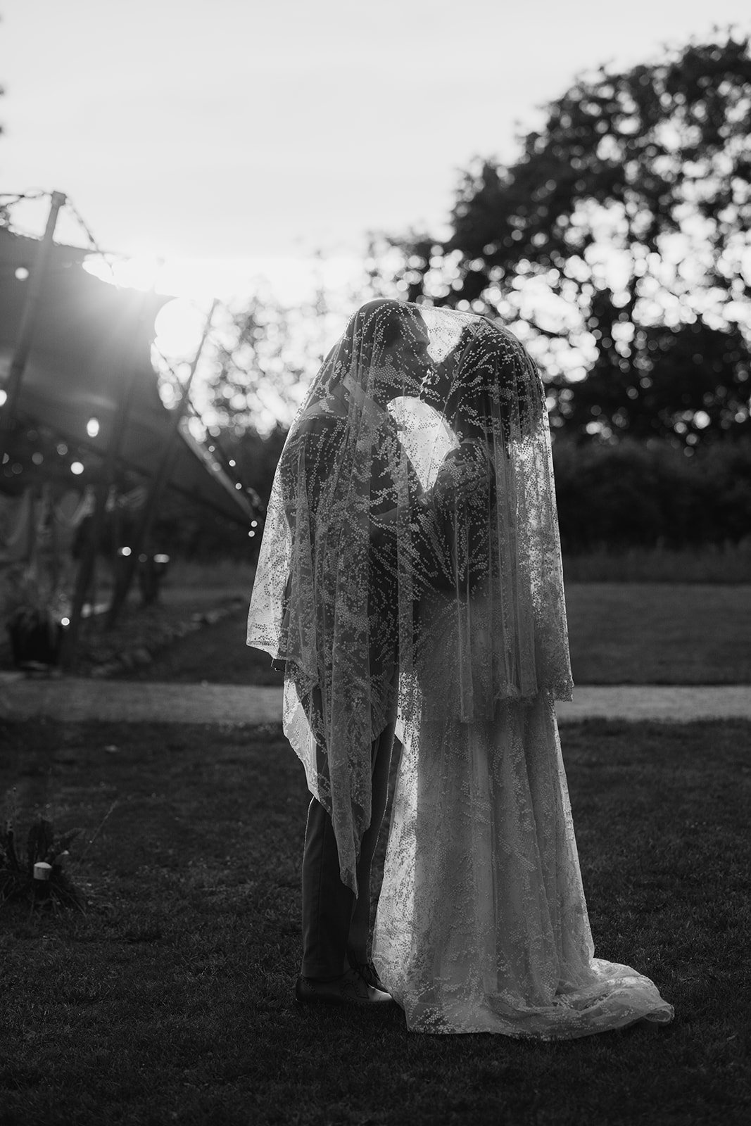 Melody & Jonny kiss beneath her lace bridal cape during a black-and-white evening portrait at Berwick Lodge in Bristol, photographed by Just James Weddings.