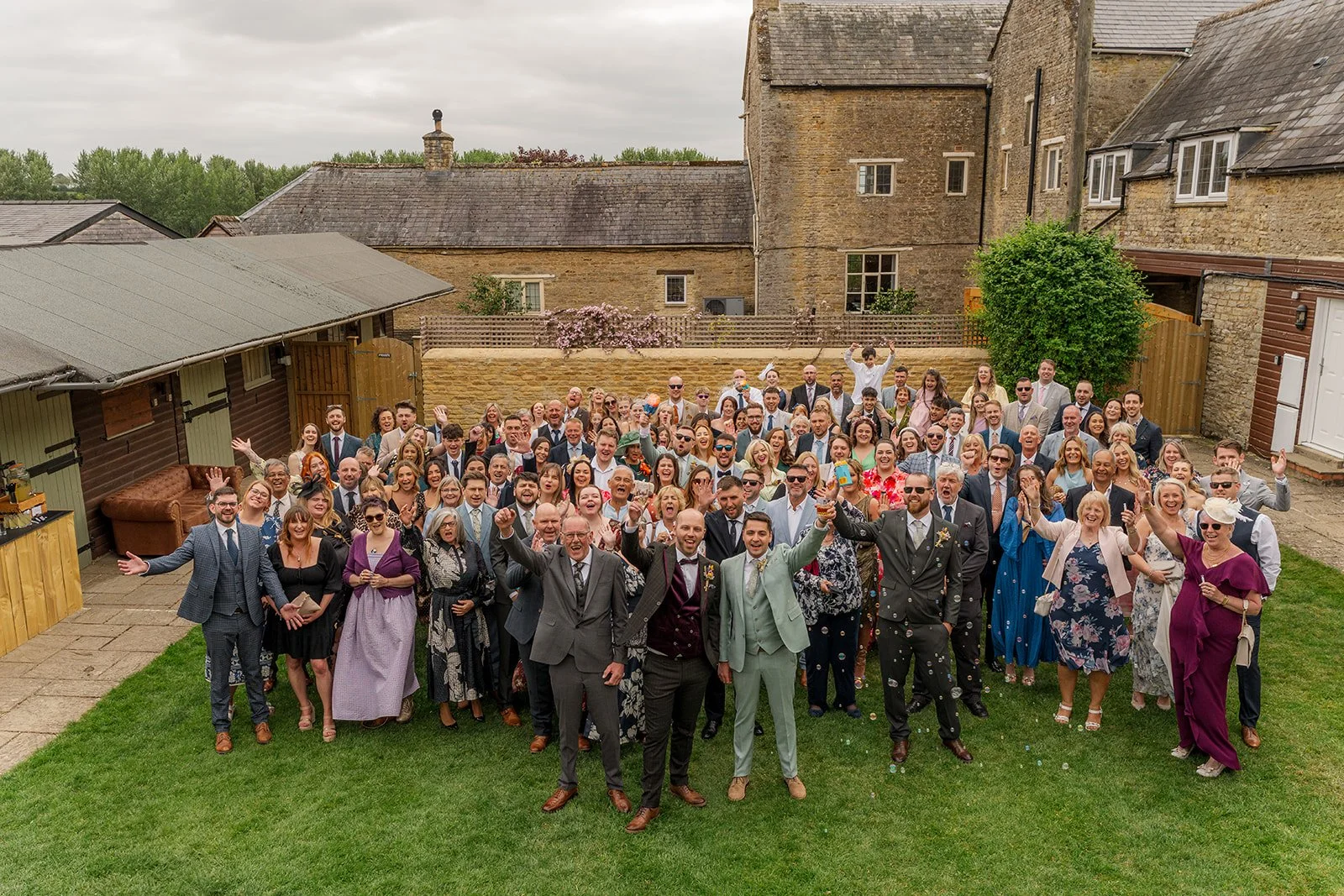 Aerial group photo of Sam & Gavin with their wedding guests at The Great Barn at Aynho in the Cotswolds, photographed by Just James Weddings after the ceremony.