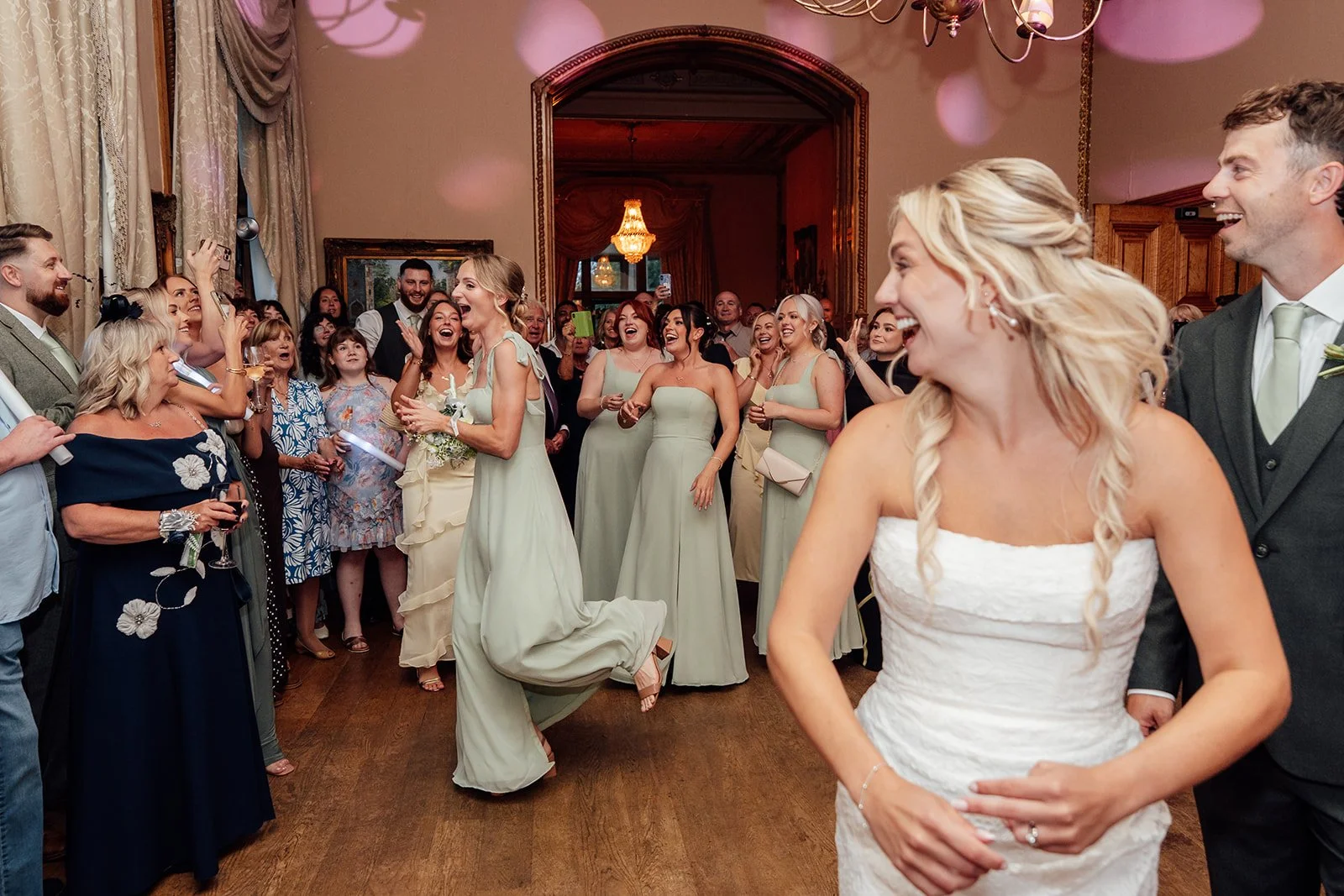 A lively bouquet toss at Orchardleigh Estate in Somerset, with Amy and Matt laughing in the foreground as guests and bridesmaids gather on the dance floor, captured by Just James Weddings.