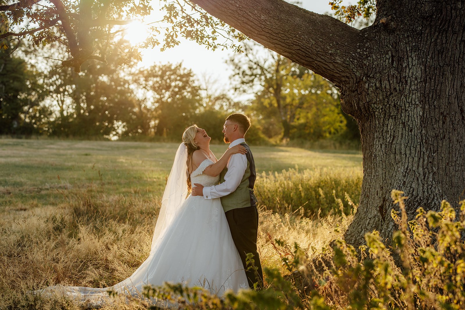 Lucy laughing with Matthew beneath a decorative parasol during golden hour portraits at Curated Canvas at Noah’s Pond in Somerset, photographed by Just James Weddings.